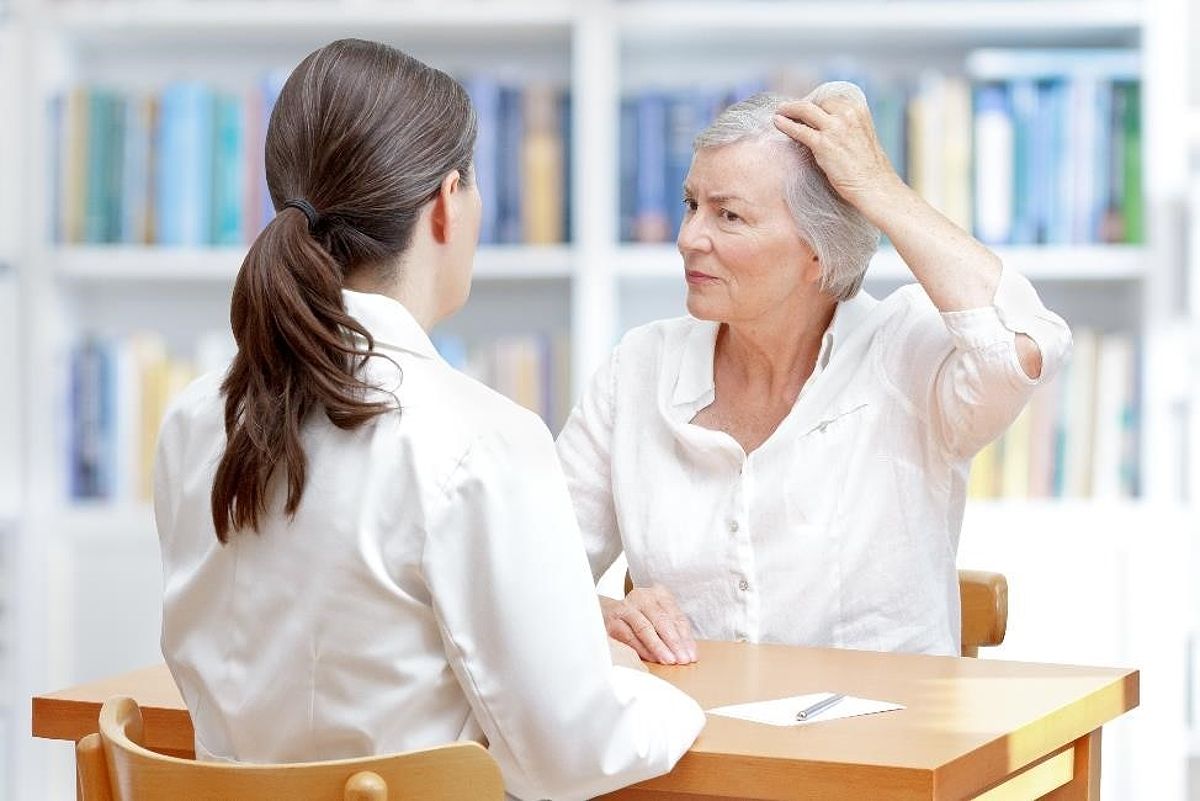 Older woman with gray hair showing her thinning hair to female doctor